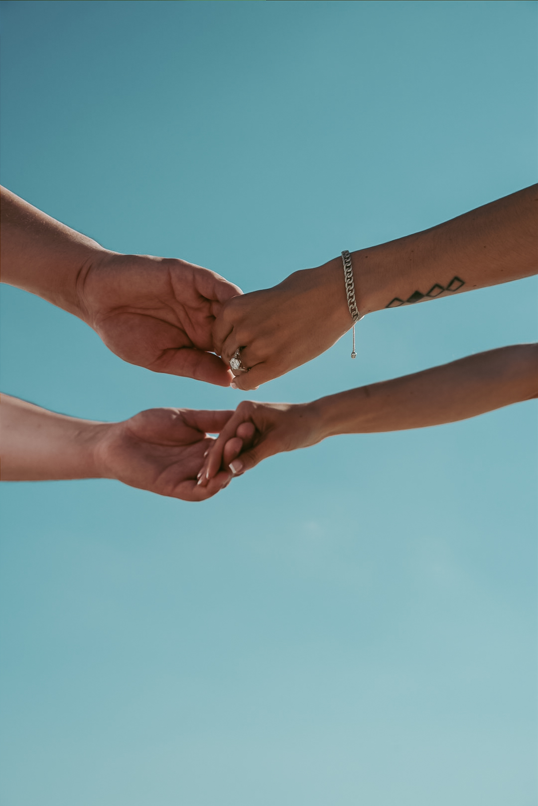 Hands reaching with engagement ring against blue sky