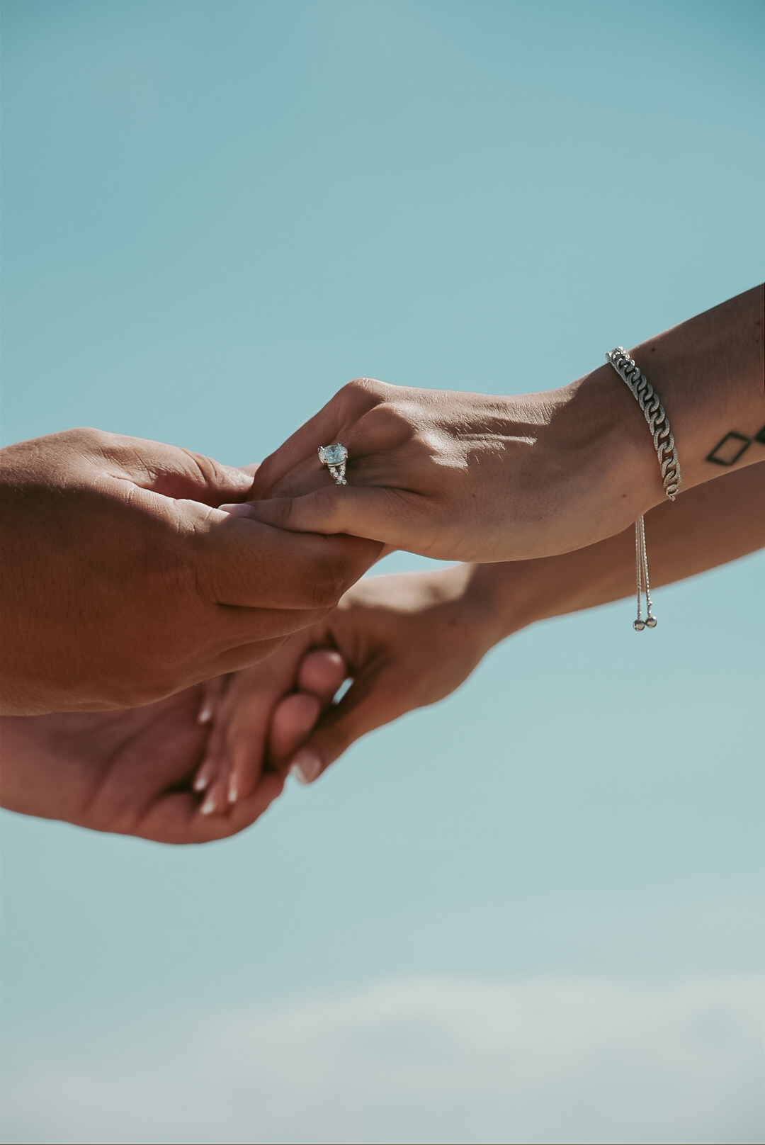 Close-up hands with ring and bracelet against blue sky